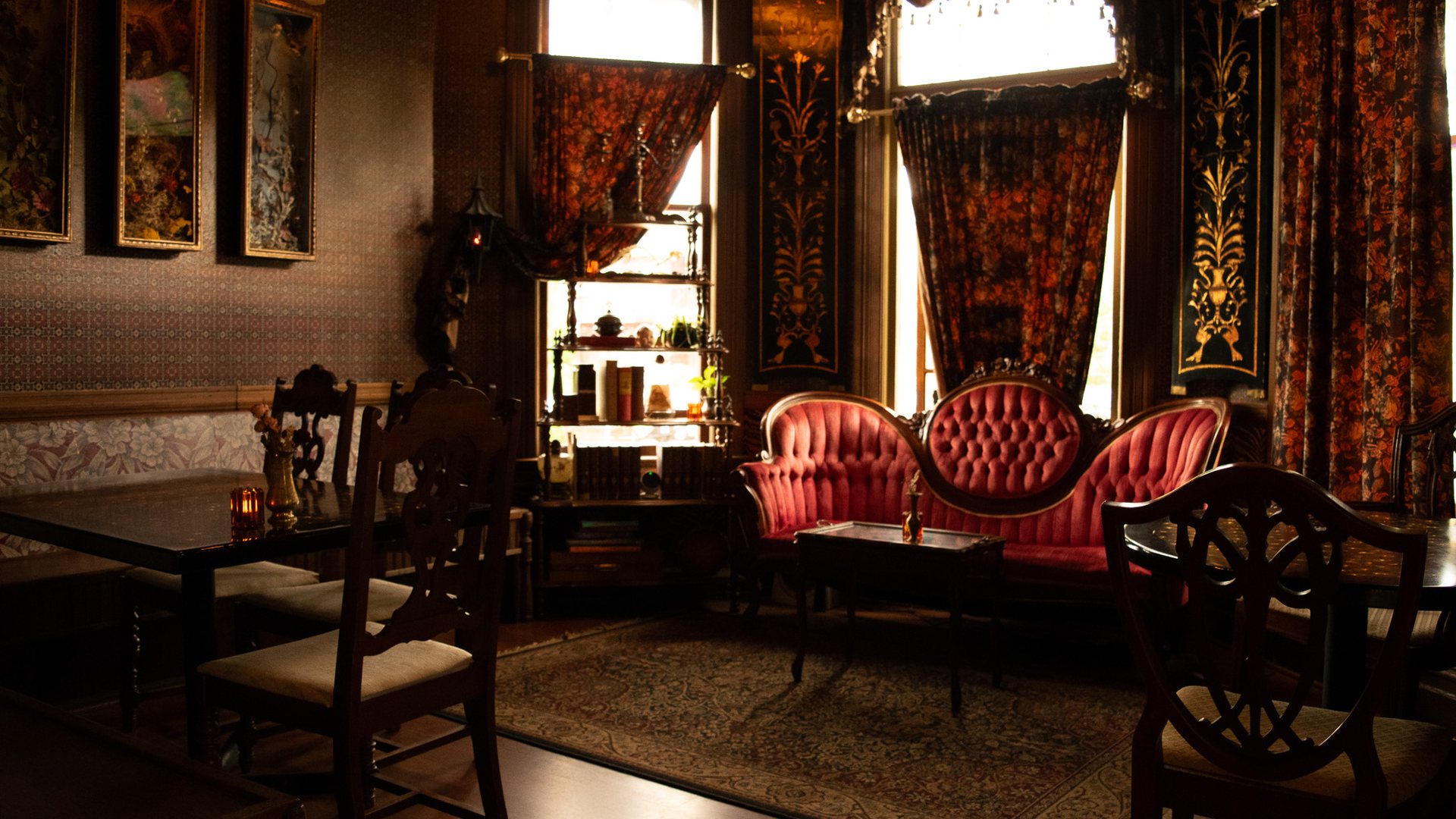 The front parlor at Foxtrot with a red tufted velvet sofa, floral drapes and gilded panels between the windows